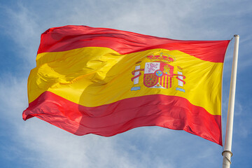 Flag of Spain, called La Rojigualda, waving on a blue sky.