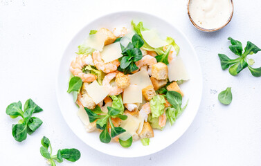 Caesar salad with shrimp, iceberg and lamb lettuce, croutons, parmesan cheese with caesar dressing. White table background, top view - obrazy, fototapety, plakaty
