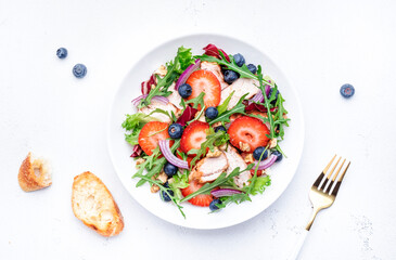 Strawberry, grilled chicken fillet and herbs healthy salad with arugula, blueberries and walnuts, white kitchen table, place for text. Fresh useful dish for healthy eating