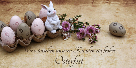 Osterkarte Frohe Ostern: Osterei mit Blumen und einer Osterhasen Figur in einer Eierschachtel mit...