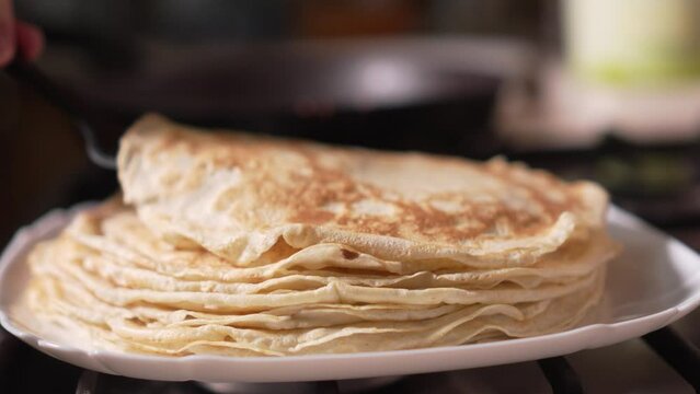Stack of thin pancakes on blurry background.Maslenitsa. Close-up pancakes. woman's hand adds new pancake from pan. Hot. Cooking pancakes at home, homemade thin pancakes.