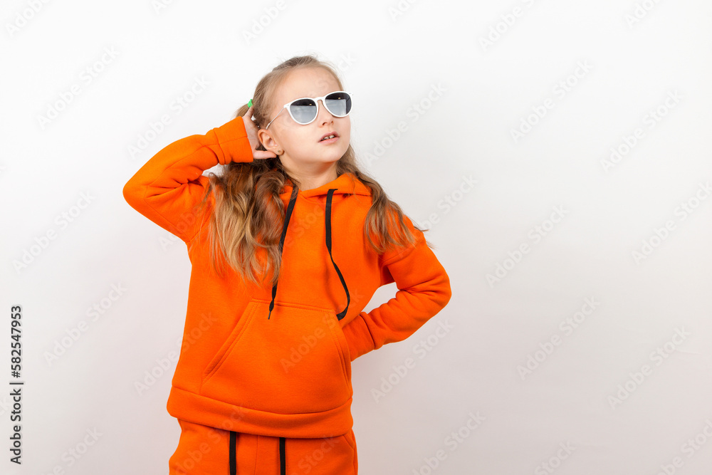 Wall mural A little girl in an orange hoody and sunglasses, emotions of joy and a sunny day, portrait. On a white background. - Wall murals