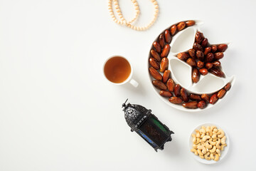 Ramadan Kareem concept. Flat lay composition with dried dates, Islamic lantern, cup of tea, rosary, nuts on white table.