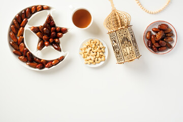 Naklejka premium Flat lay composition with Arabic lantern, dried dates, nuts, cup of tea, rosary on white background. Ramadan Kareem concept.