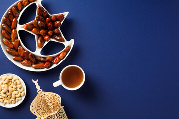 Ramadan Kareem greeting card template. Dried dates in Islamic star and crescent bowl, wooden oriental lantern, nuts, cup of tea on table.