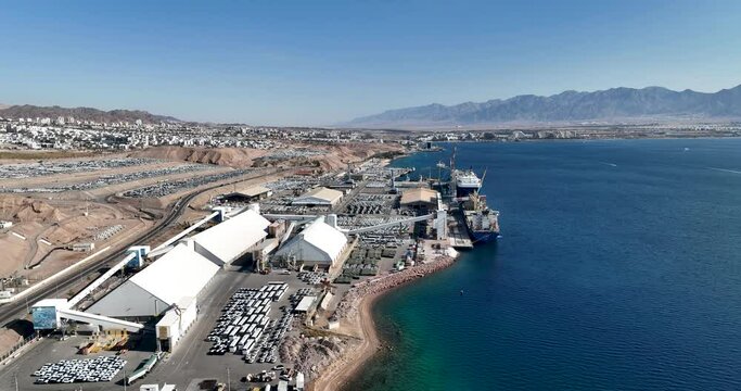 Aerial footage of Eilat sea port in the red sea. Cargo ships anchor in the port and Thousands of vehicles park in and around the port. Filmed in C4K Apple ProRes 422 HQ