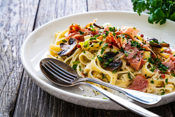 Tagliatelle with cooked ham, parmesan cheese and white mushrooms served on wooden table 