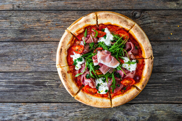 Pizza parma - prosciutto di parma, arugula, mozzarella, tomatoes, burrata on wooden table