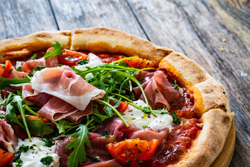 Pizza parma - prosciutto di parma, arugula, mozzarella, tomatoes, burrata on wooden table