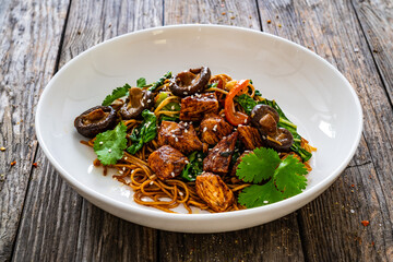 Asian food - chicken nuggets, noodles, stir fried vegetables, soy sauce, pak choi cabbage and shiitake mushrooms on wooden table 