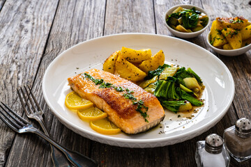 Fried salmon steak with lemon, fried potatoes and pak choi cabbage served on wooden table
