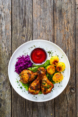 Barbecue chicken drumsticks with fried potatoes, lettuce and ketchup on wooden table
