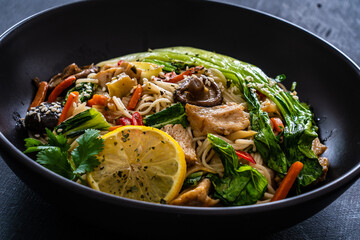 Asian food - chicken nuggets, noodles, stir fried vegetables, soy sauce, pak choi cabbage  and shiitake mushrooms on wooden table
