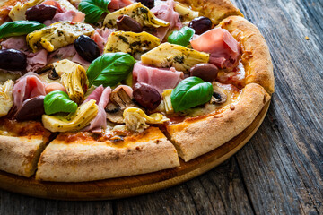 Pizza capricciosa with cooked ham, mozzarella, artichoke   and vegetables on wooden table
