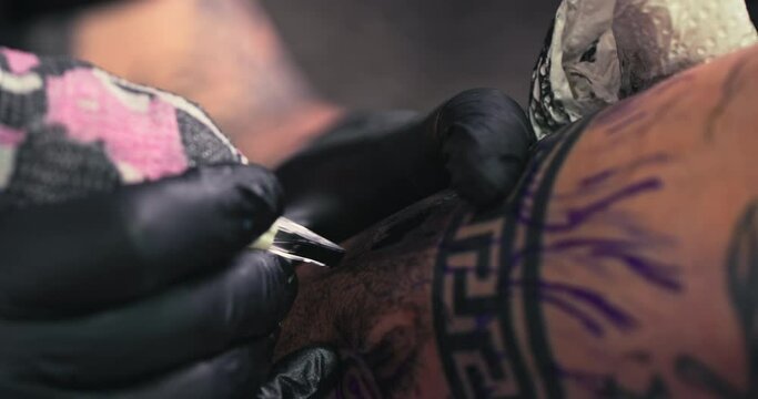  Close up tattoo artist shows the process of getting black tattoos with paint. The master works in black sterile gloves. Master tattoo artist in studio.