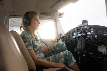 Woman pilot in military uniform pre-flight checking inside on a small aviation airplane. Flight pre-check inspection.