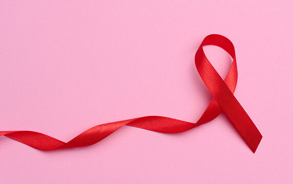 A silk red ribbon in the form of a bow on a pink background, a symbol of the fight against AIDS and a sign of solidarity and support