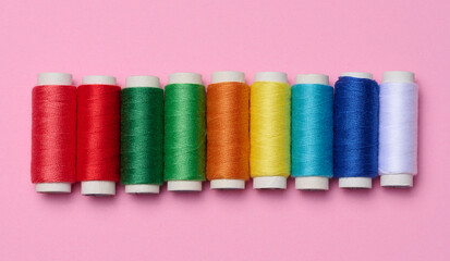 Multicolored spools of sewing threads on a pink background, top view