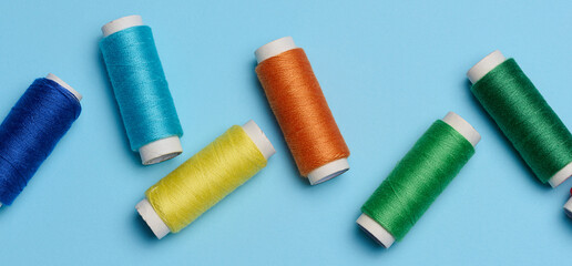 Multicolored spools of sewing threads on a blue background, top view