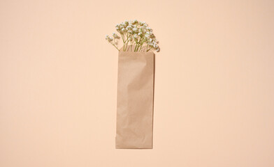 Bouquet of white gypsophila in a brown kraft paper bag on a beige background, top view