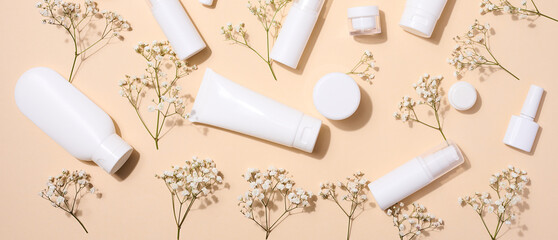 White plastic tubes, jars, and gypsophila branches on a beige background, containers for cosmetic creams and gels, advertising and brand promotion, top view