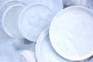 Dishes and bowls in water and bubbles of dishwashing liquid