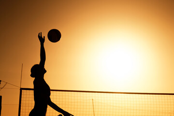 Silhouette woman playing beach volleyball on sunset.