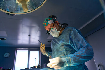 surgeon in the operating room is standing at the table with the patient under the lamp