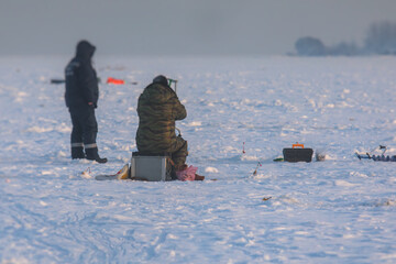 Process of ice fishing, group of fishermen on ice near tent shelter, with equipment in a winter...