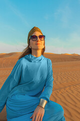Beautiful woman in blue dress among the Dubai desert at sunset time.