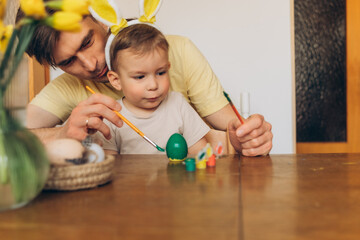 dad and child in bunny ear headbands decorating eggs for Easter