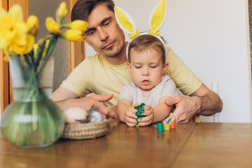 Fototapeta premium dad and child in bunny ear headbands decorating eggs for Easter