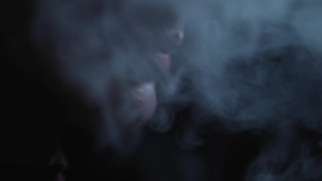 Electric device for smoking. A man smokes an electronic cigarette in the dark. Vape. E-cig, vsping. Concept: the harm of smoking. Slow motion, smoke on a dark background, A man without a face holds an