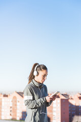 Fototapeta na wymiar Young girl with music headphones looking at her cell phone while wearing sportswear