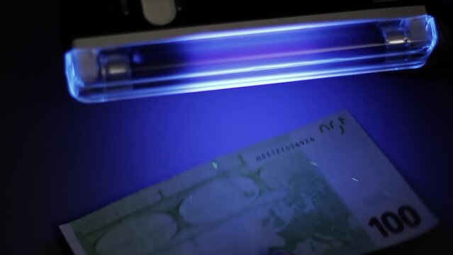 A man checks the authenticity of a hundred Euro banknote under a UV lamp