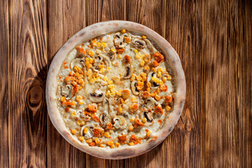 Appetizing pizza on a creamy sauce with mushrooms, corn, chicken fillet and mozzarella cheese on woden background
