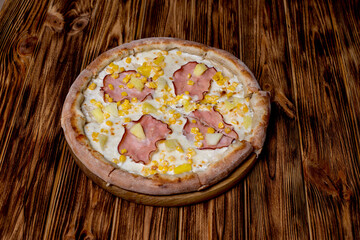 Delicious pizza with ham, pineapple, corn on a creamy base on woden background. Hawaiian pizza