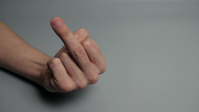 Male hand shows the middle finger, close-up on a gray background. Frustrated, angry and conflict expression for fuck you while asking person to leave copy space. An insulting gesture.
