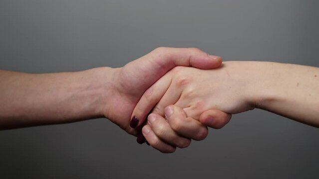 Close up of male and female hands shaking. Man and woman greeting and making deal. Man and woman greet each other with a friendly gesture gesture. Handshake gesture on a gray background.
