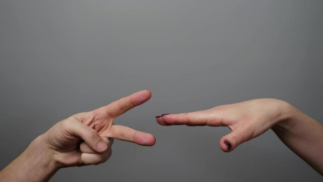 Friendship, dealing with conflict, having fun. Hanging out. Rock paper scissors being played by young man and woman. Close up view female and male hands playing stone, scissors and paper on gray backg