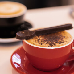 Chocolate cappuccino in red cup with a chocolate spoon. A black white in the scene.