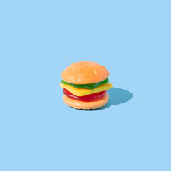 Hamburger shaped gummy candy with sunlight shadows on blue background.