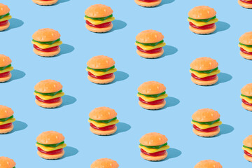 Hamburger shaped gummy candy with sunlight shadows on blue background. Summer dessert pattern.