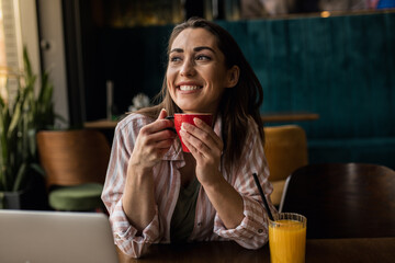 Woman looking in the distance while drinking coffee and orange juice, working remotely from a restaurant