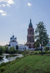 Fototapeta na wymiar The ancient bell tower of the Intercession Church with a reflection in the river among green trees on a sunny summer day in Yuriev-Polsky russia