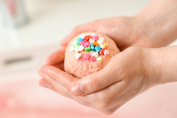 Woman with bath bomb above water, closeup