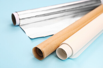Rolls of baking paper and aluminium foil on color background, closeup