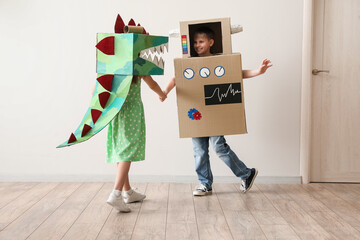 Little children in cardboard costumes playing near light wall