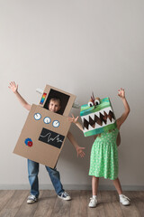 Little children in cardboard costumes playing near light wall