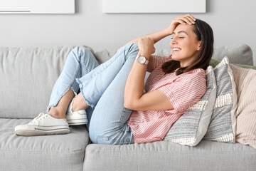 Young woman with stylish wristwatch lying on sofa at home